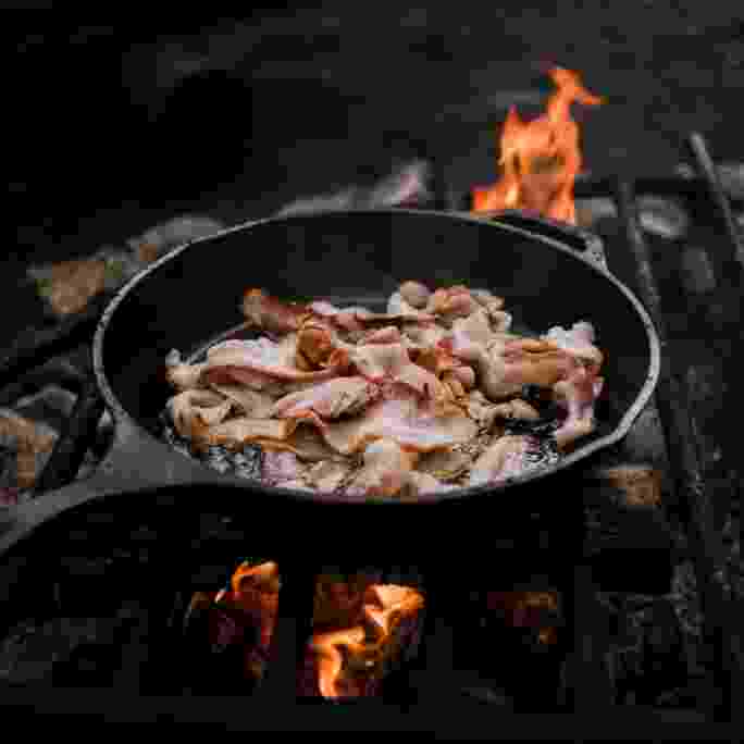 Bacon cooking in cast iron pan on camp fire